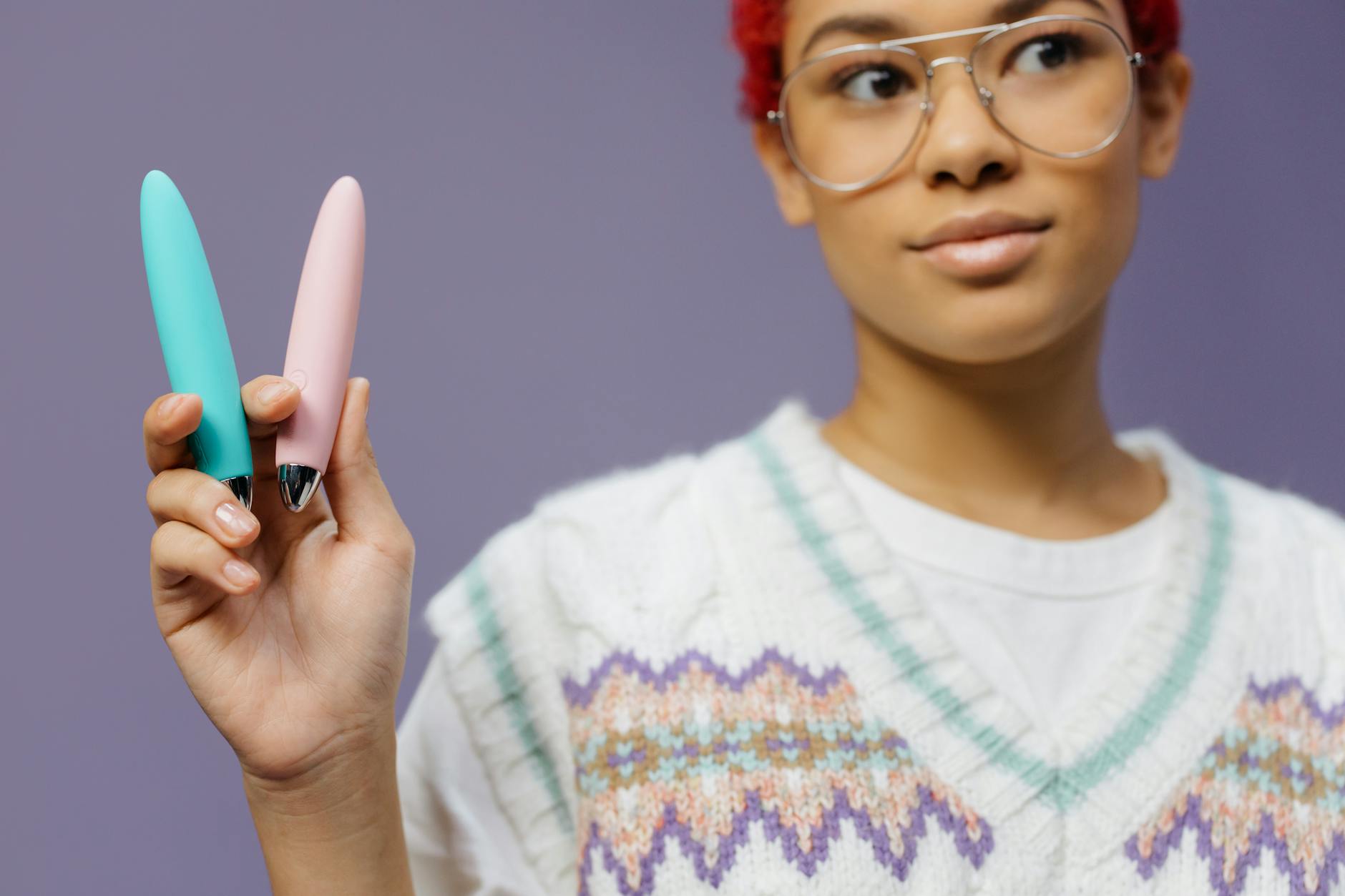 Woman holding colorful vibrators against a purple background, representing solo pleasure and self-care during relationship challenges